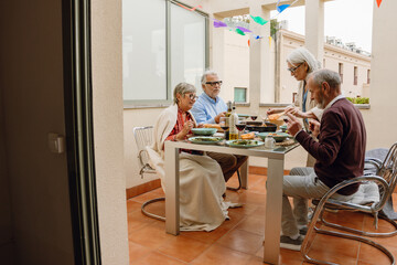 A group of three friends are sitting at a table while a female friend stands next to them holding a fork in a frying pan