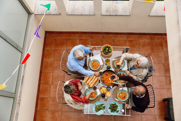 Group of four friends holding glasses and talking while sitting on chairs at a table