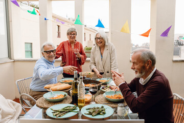 A group of four friends are talking and laughing while two of them are standing and holding glasses and two are sitting at a table