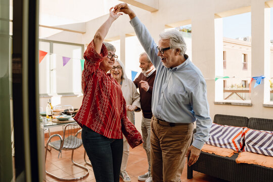 A man is talking and holding the hand of a woman who is spinning while they dance with two friends - Powered by Adobe