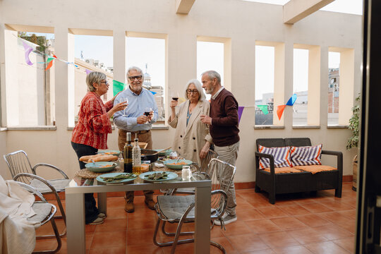 A group of four friends are holding glasses and standing at a table while two of them are talking and one is smiling