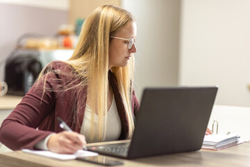 Woman working from home with laptop and paperwork, focused on organizing documents at her desk