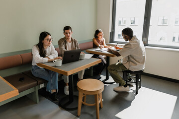 Male and female workers looking at a laptop while a male and female workers sitting next to them holding a pen and talking while they sit at a table