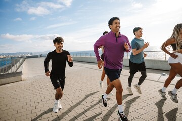 Group of three male athletes smiling and running near two female athletes