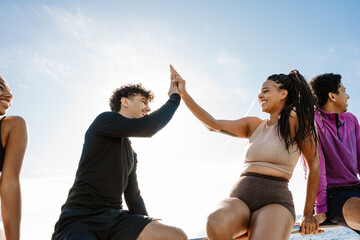 Male and female athletes giving each other high five and laughing while sitting on a fence