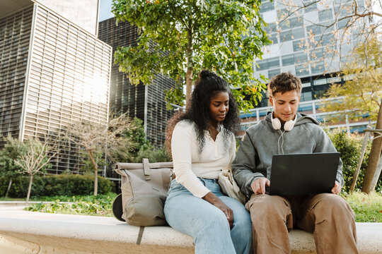 Male and female students sitting and looking at the laptop he is holding and talking