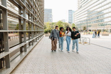 Obraz premium A group of four students walk and laugh while looking at a phone that one of them is showing
