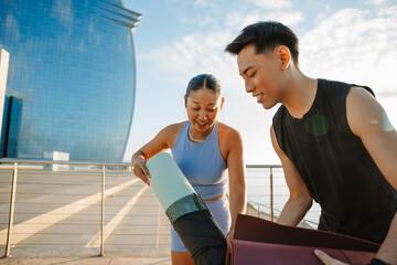 A woman takes a mat out of its cover while standing next to a man and they laugh