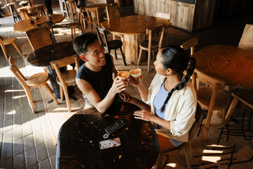 A man laughs and clinks cups with a woman sitting next to him at the table
