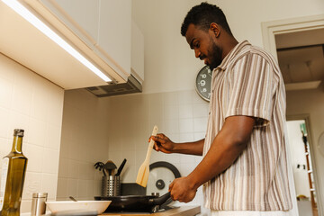 A man is smiling and standing while holding a spatula over a frying pan