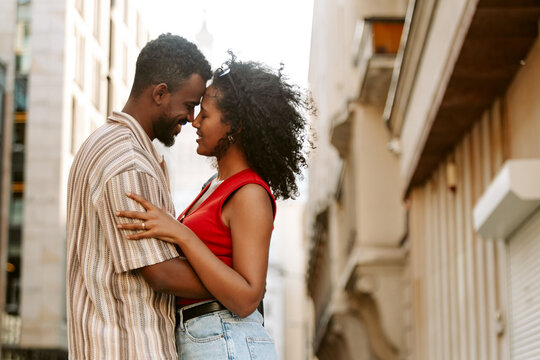 A man hugs a woman who has her hand on his arm as they stand close together and smile