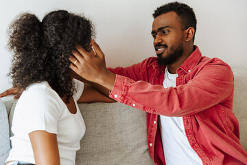 Man talking and fixing woman's hair while they sit on couch