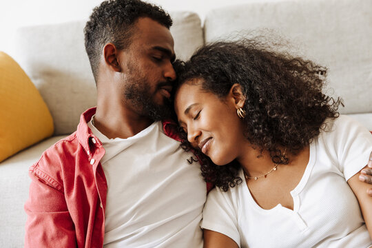 Man hugs woman who leans on him while they recline on sofa with eyes closed - Powered by Adobe