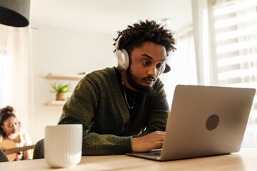 Male musician looking at laptop and listening to headphones while sitting at table