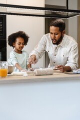 Daughter listens to father talking and pouring flour while standing next to her at the table