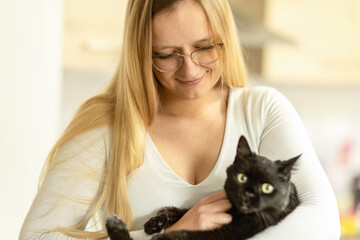 Woman cuddling a black cat at home, tender moment between pet and owner in warm indoor light