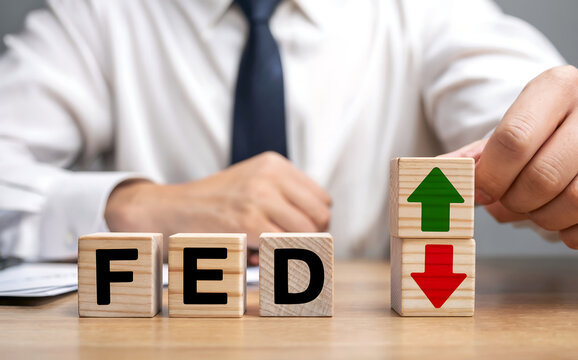 Closeup of a businessmans hands arranging wooden blocks with letters spelling fed and arrows indicating upward and downward trends, representing federal reserve economic policy and market fluctuations - Powered by Adobe