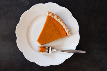 A slice of pumpkin pie with a fork holding the first bite, dark background