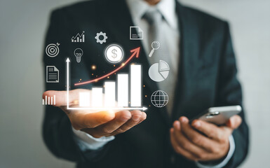 A businessman in a suit holding a smartphone displays a glowing infographic with a rising bar chart and business icons, representing data analysis and growth