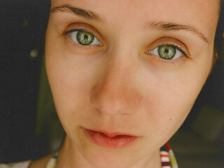 Close-up portrait of a young woman with expressive green eyes and natural skin texture. Minimalist lighting and soft tones create a modern aesthetic suitable for beauty, wellness, lifestyle themes.