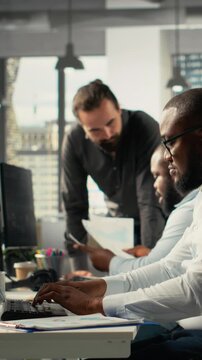 Vertical Video Colleagues in multinational company office discuss strategy, charts and analytics on laptop or files. Work team coordinates progress, insights and documentation for better outcomes