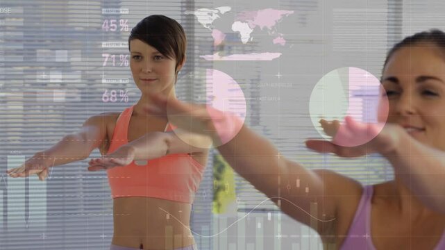 Two women raising arms in fitness studio on cue, animated charts tracking wearable sensor data