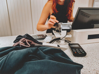 Shopping experience at a retail checkout counter. A cashier processes a purchase while clothing items and a payment terminal are in the foreground. Trendy concept of sales, retail, customer service.