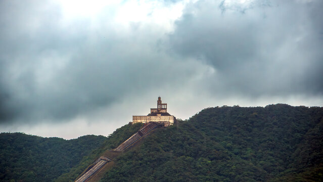 Mountain hydroelectric facility with long penstocks rising through lush green hills under dramatic storm clouds