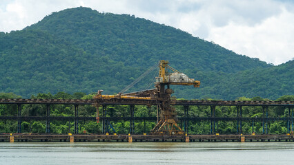 Old massive decaying industrial loader on a concrete pier in a tropical bay, set against a backdrop...