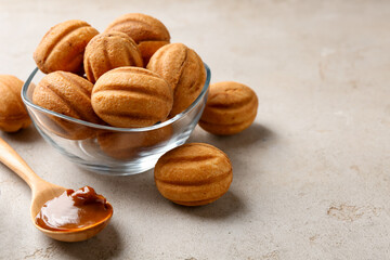 Delicious nut shaped cookies with boiled condensed milk and spoon on light textured table, closeup....