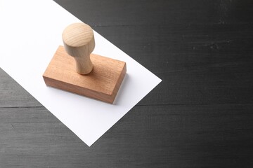 One wooden stamp and blank sheet of paper on black table. Space for text