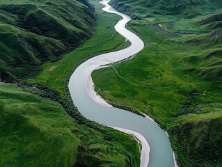 An aerial view captures a wide, winding river flowing through vibrant green, rolling hills and valleys. The landscape is illuminated by soft daylight, creating