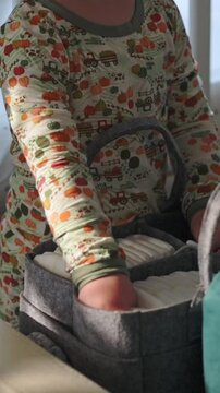 vertical screen infant carefully selects diaper from storage, young child gently reaches for neatly stored diaper options, little one calmly and cautiously picks diaper from organized