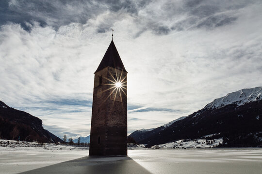 Sunken Church Tower of Curon with Winter Sunstar at Lake Resia, South Tyrol, Italy