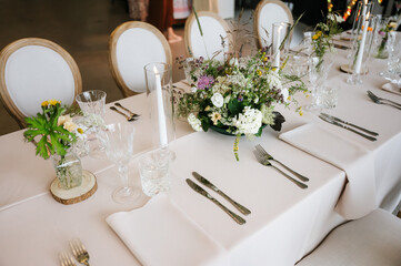 Elegant wedding table setting with wildflower centerpieces, crystal glassware, and soft neutral linens, creating a natural, romantic, and refined reception atmosphere.