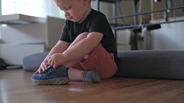 child practicing lace, small child focused on learning to tie shoelaces independently, determined young child concentrating on practicing shoe laces while seated confidently on wooden floor child