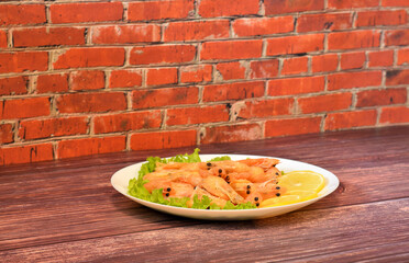 A plate of freshly cooked shrimp on a lettuce leaf with ripe lemon slices on a wooden table.