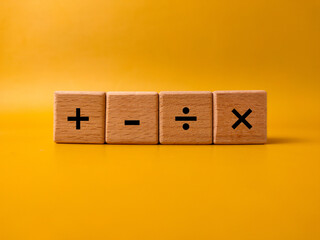 The image displays four wooden blocks with basic mathematical operation symbols on a yellow background