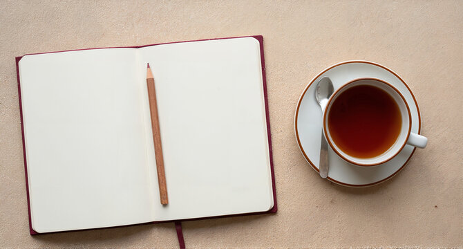 Open notebook with blank pages and a cup of tea on a textured beige surface top view