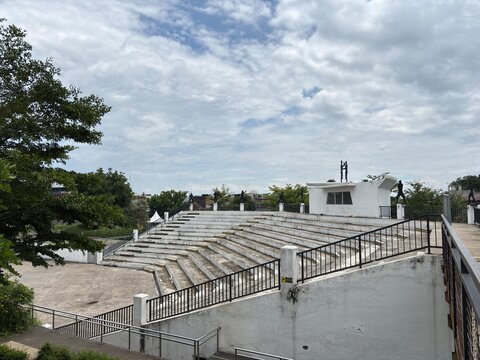 White concrete amphitheater with terraced seating and black railings, offering an elevated view under a cloudy sky, a spot for performances or relaxation.