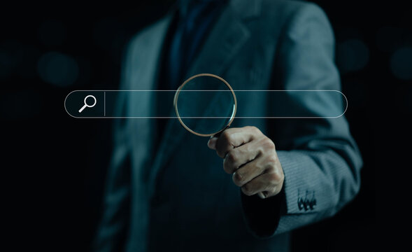 A business professional holding a magnifying glass in front of a digital search bar, symbolizing online searching, data analysis, keyword research, investigation, and modern information discovery.