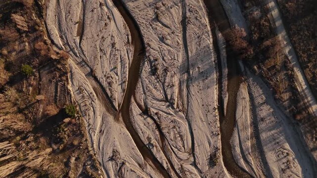 High-angle top down view of a dry braided riverbed near Wanaka, New Zealand. Golden sunset light creates textures on the gravel and sand channels. Ideal as an abstract nature background