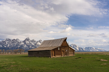 Clouds paint the sky above the barn, highlighting the majesty of the Teton Range.