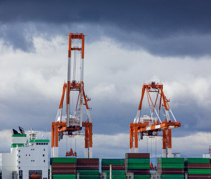 Lowered arm of a gantry crane's lifting mechanism positions to move container in shipping yard featuring two towering cranes.