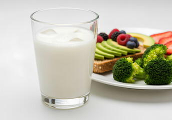 Close-up of a glass of milk with ice cubes placed next to a plate featuring a healthy breakfast or snack.