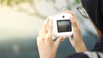 Hands Holding a White Instant Camera Outdoors Against a Bright Golden Hour Sun Flare