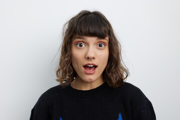 Portrait of a young woman with dark hair and bangs, expressing surprise with wide eyes and an open...