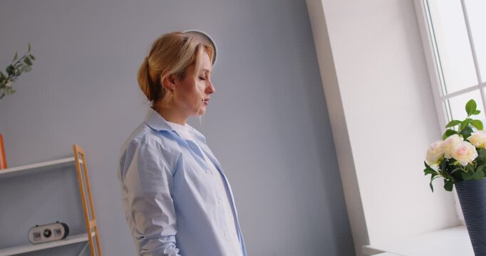 Portrait of young woman suffering from dizziness standing alone in living room at home feeling unhealthy and losing consciousness. Female person fainting. Healthcare concept. 4k video. Slow motion.