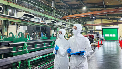 防護服を着て工場の中を歩く男女作業員