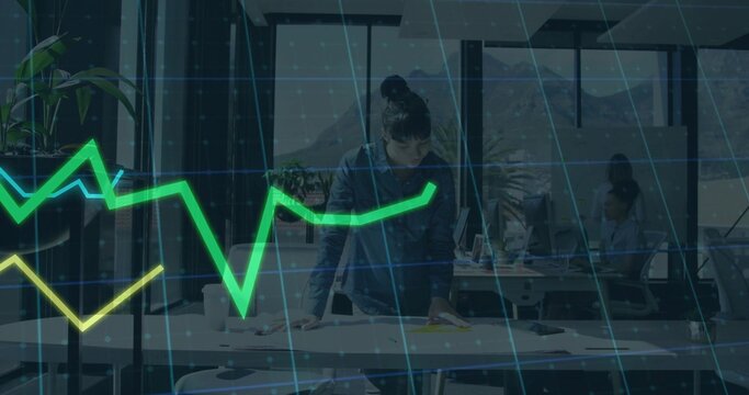 Leaning central woman in dark button-up shirt reviewing papers at open-plan office, with charts - Powered by Adobe